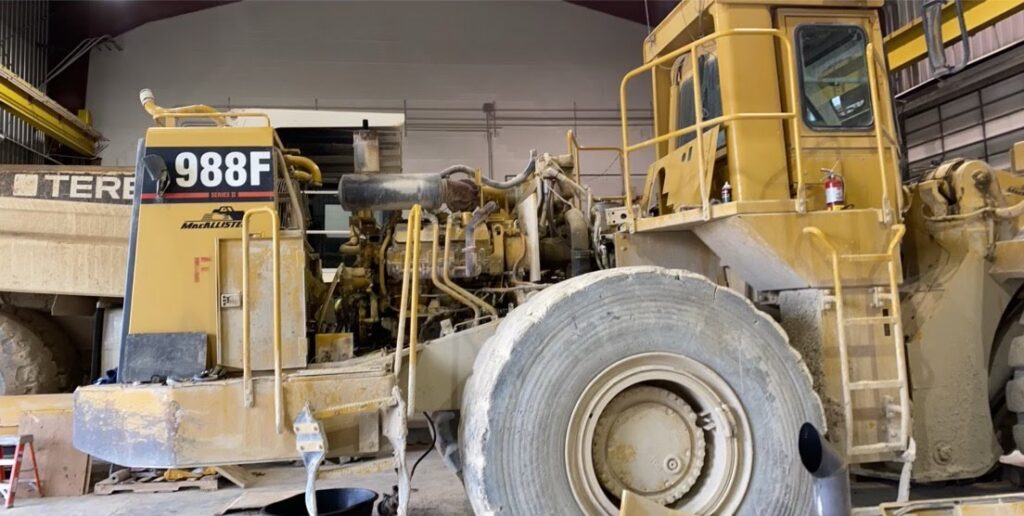 Similar to the second photo, it shows the engine being maneuvered into place, with a focus on the front of the loader, where the engine will be installed.