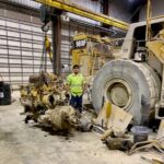 Brian is standing next to the removed engine, which is placed on the ground. The size of the engine in comparison to Brian gives an idea of the scale of the operation and the size of the machinery involved.