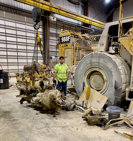 Brian is standing next to the removed engine, which is placed on the ground. The size of the engine in comparison to Brian gives an idea of the scale of the operation and the size of the machinery involved.